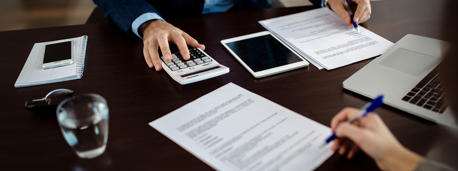 Spotkanie biznesowe przy umowach i&nbsp;kalkulatorze ilustrujące koszt obsługi prawnej firmy w&nbsp;modelu ryczałtowym, godzinowym i&nbsp;mieszanym